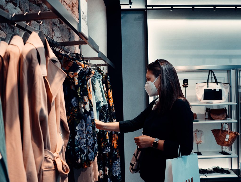 A woman wearing a face mask looks at clothing for sale in a department store